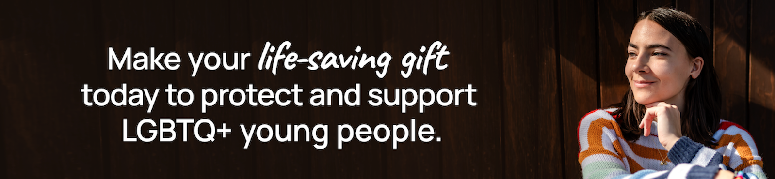 A photo of an LGBTQ+ young person sitting against a wood-paneled wall. Make your life-saving gift today to protect and support LGBTQ+ young people.